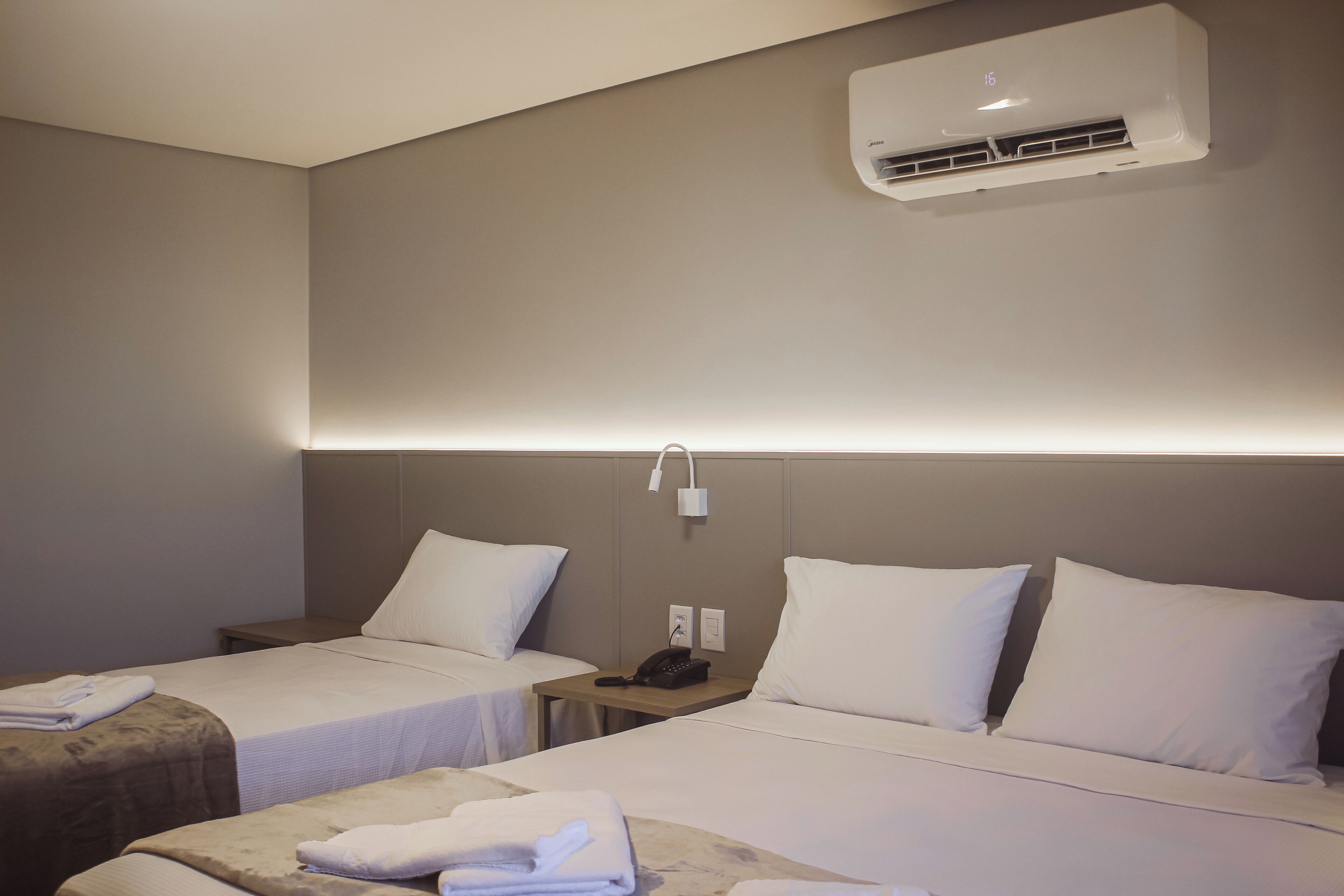 Habitación de hotel con dos camas, una mesita de noche con teléfono y un equipo de aire acondicionado en la pared.