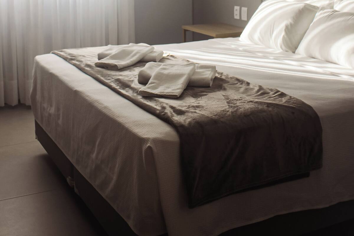 Una habitación de hotel con una cama bien hecha, una mesita de noche y una ventana con cortinas.