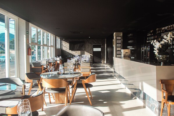 A modern restaurant with a long counter, wooden chairs, and tables.