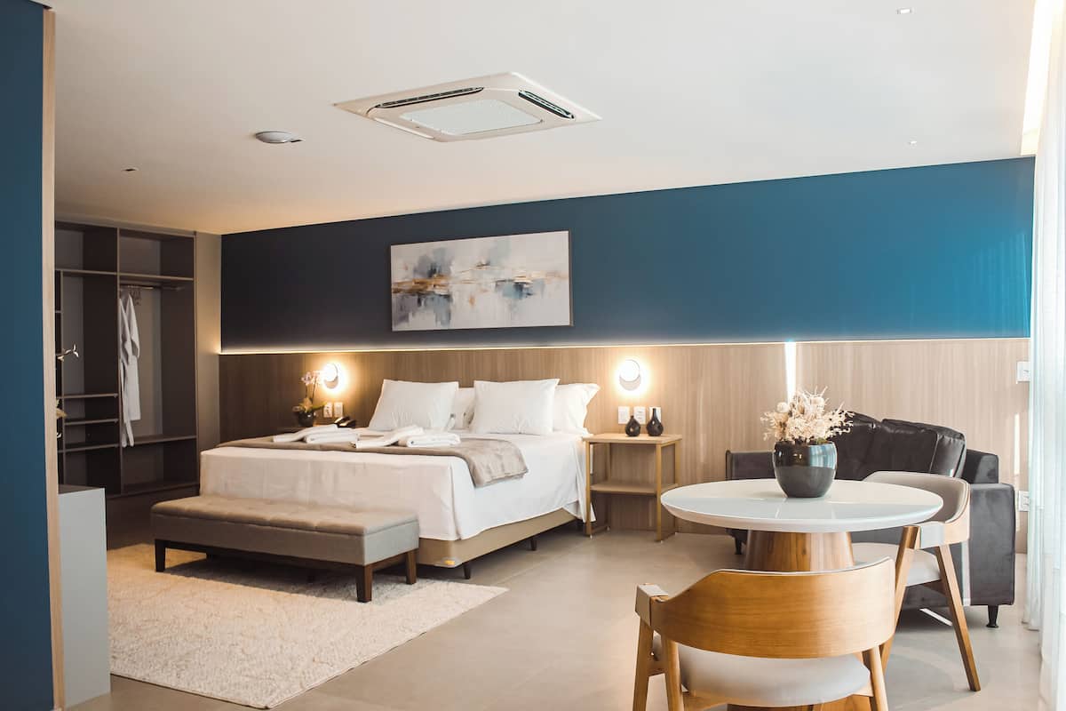 Un dormitorio moderno con cama, mesitas de noche, una mesa de comedor redonda y un espacio de estar.