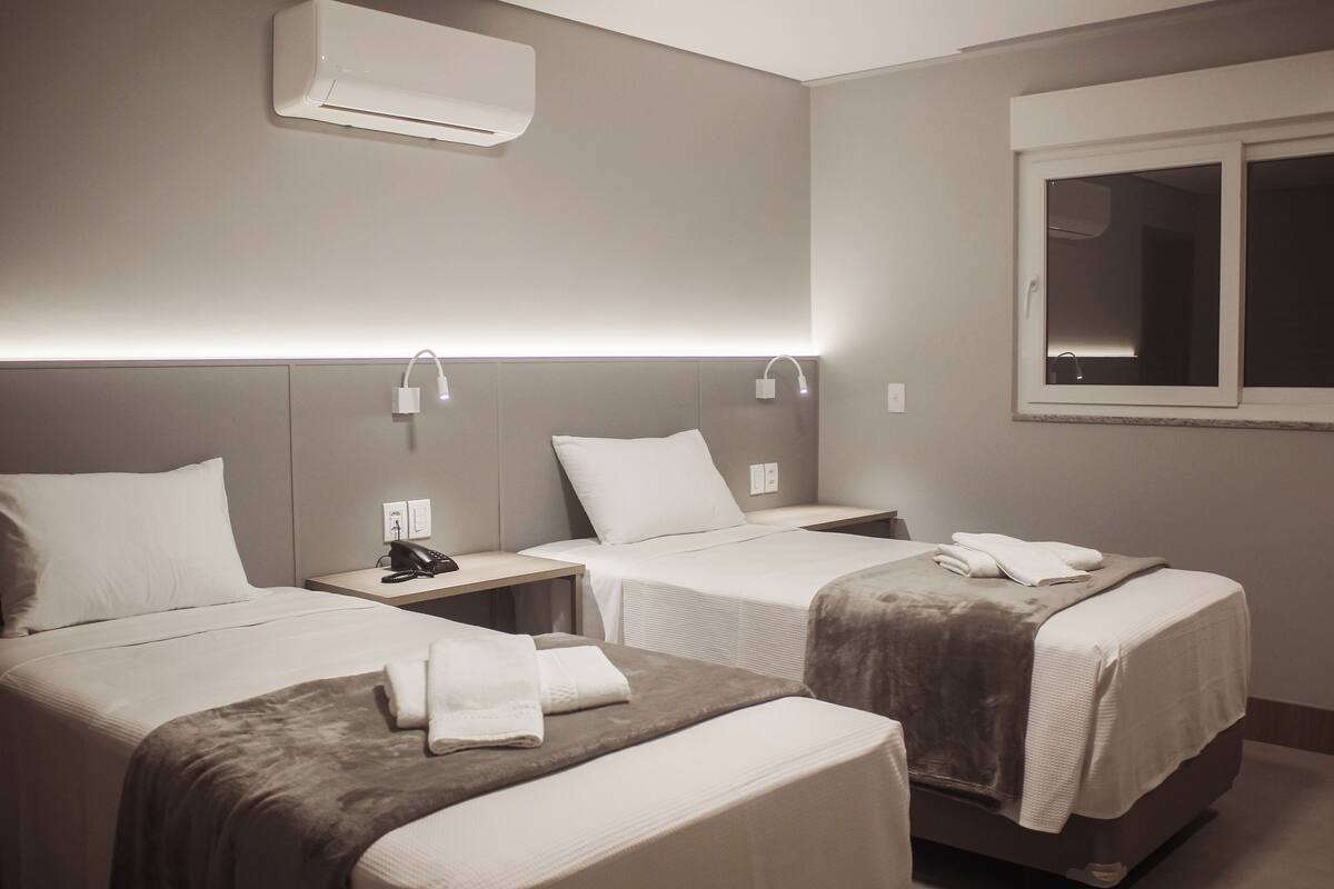 Habitación de hotel con dos camas, una mesita de noche con teléfono y un equipo de aire acondicionado en la pared.