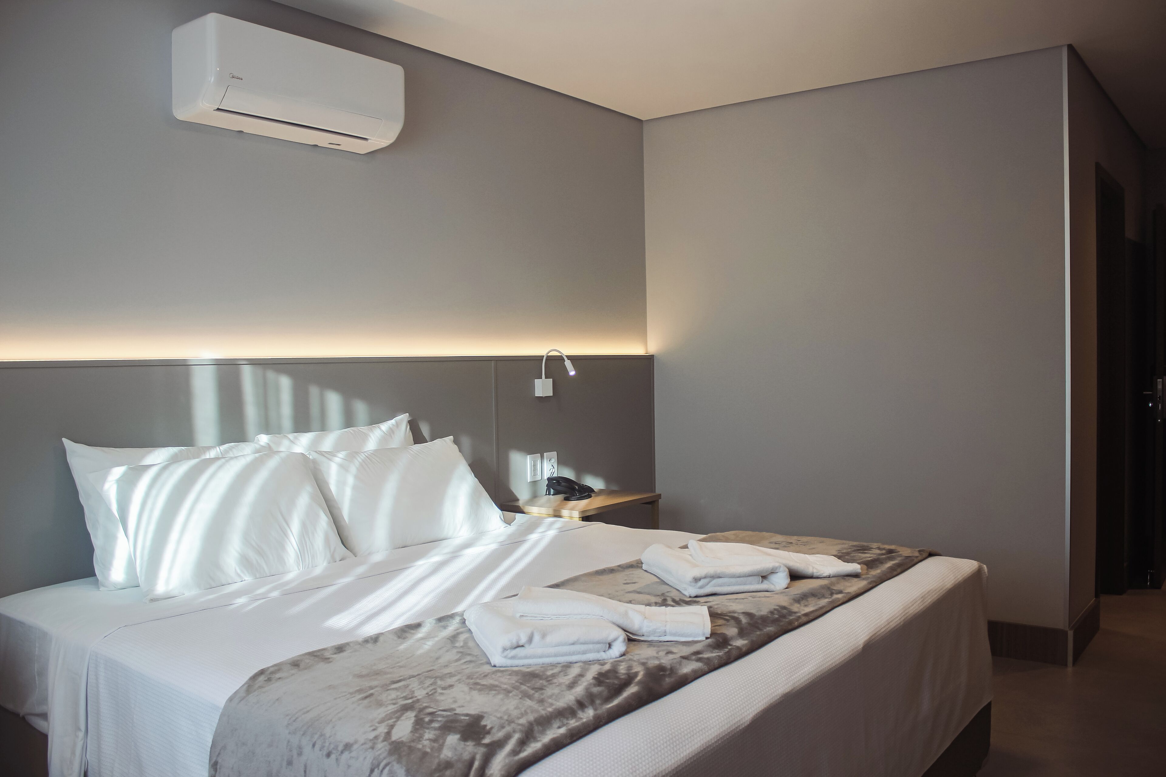 Une chambre d’hôtel avec un lit bien fait, une table de chevet avec une lampe et un appareil de climatisation fixé au mur.