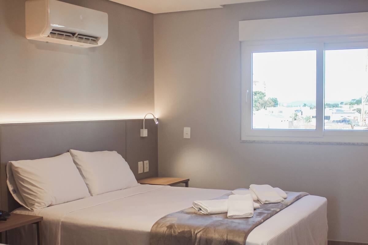 Habitación de hotel con dos camas, ventana, aire acondicionado y mesita de noche con lámpara.