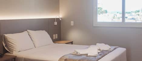 Habitación de hotel con dos camas, ventana, aire acondicionado y mesita de noche con lámpara.