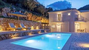 A swimming pool with stone walls and lounge chairs, surrounded by a two-story building with balconies.
