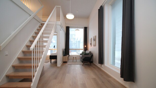 Un intérieur moderne avec un escalier en bois, un canapé et une grande fenêtre agrémentée de rideaux.