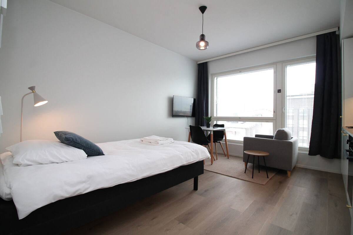 Ein modernes Hotelzimmer mit einem großen Bett, einem Schreibtisch, einem Sessel und einem Fernseher an der Wand.