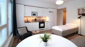 Une chambre d’hôtel compacte comprenant un coin cuisine, un lit, une chaise et une petite table agrémentée d’une plante.