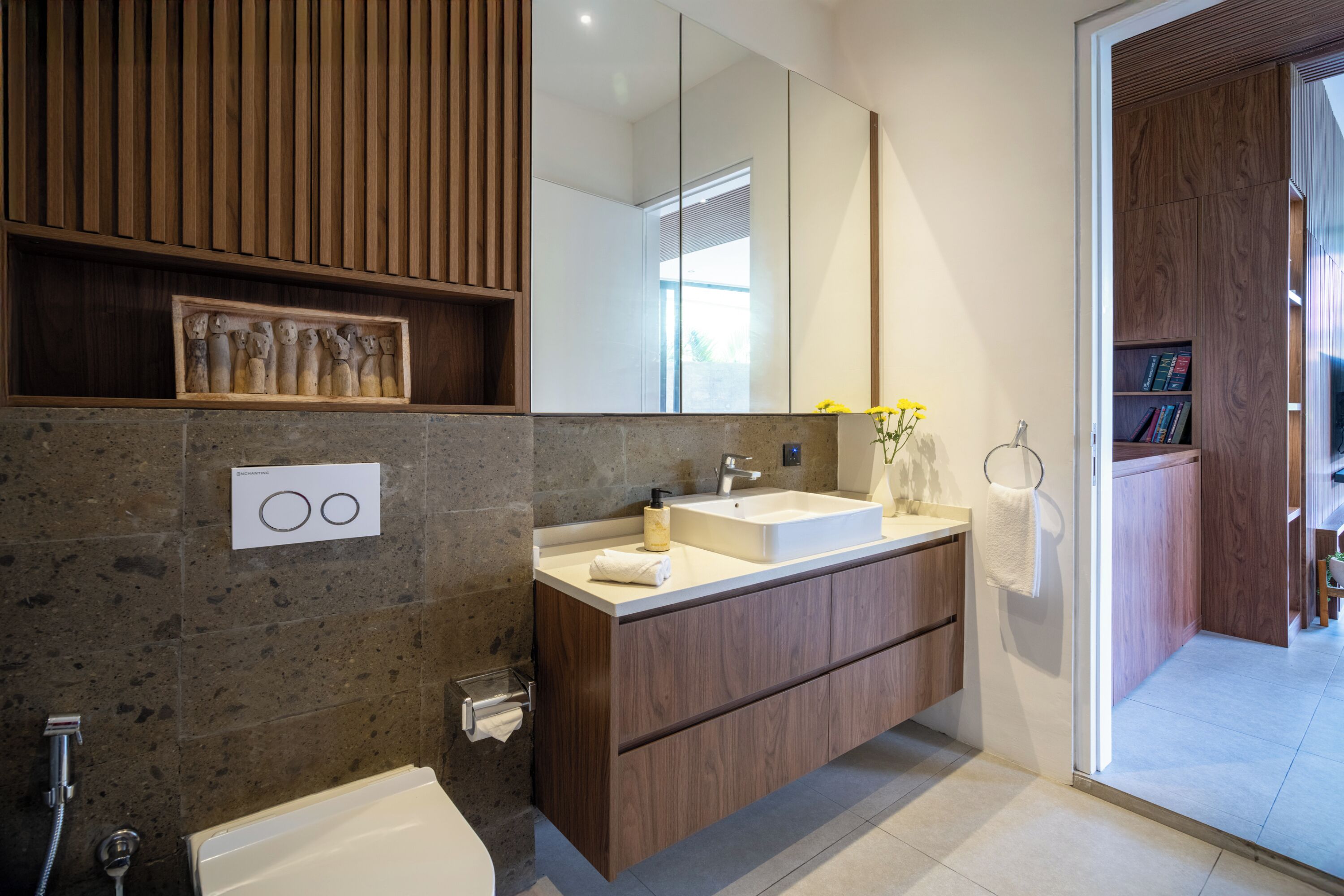 A modern bathroom with a stone wall, wooden vanity, and a large mirror.