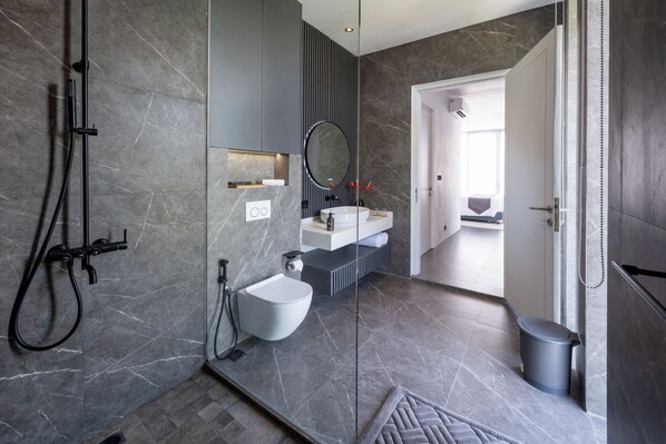 Un baño moderno con cabina de ducha de vidrio, un lavabo blanco y un bidé.