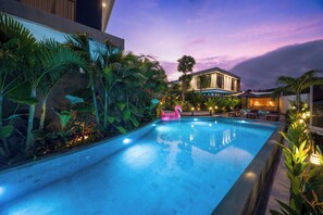 Una piscina con un flotador rosa con forma de flamenco, rodeada de exuberante vegetación tropical y un edificio moderno al fondo.