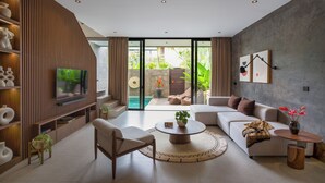 Una sala de estar moderna con un televisor grande, un sofá, una mesa de centro y vistas a una piscina.