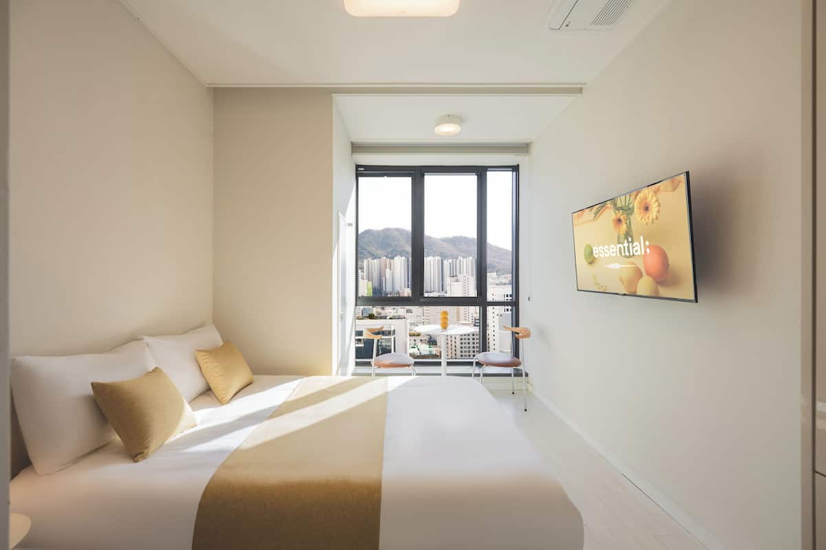 Une chambre d’hôtel avec un grand lit, un téléviseur fixé au mur et un balcon offrant une vue sur la ville.