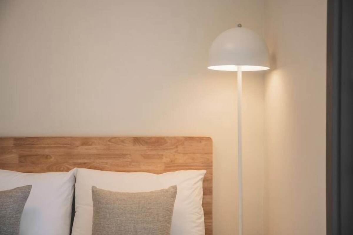 A bed with a wooden headboard, white and gray pillows, and a white floor lamp.