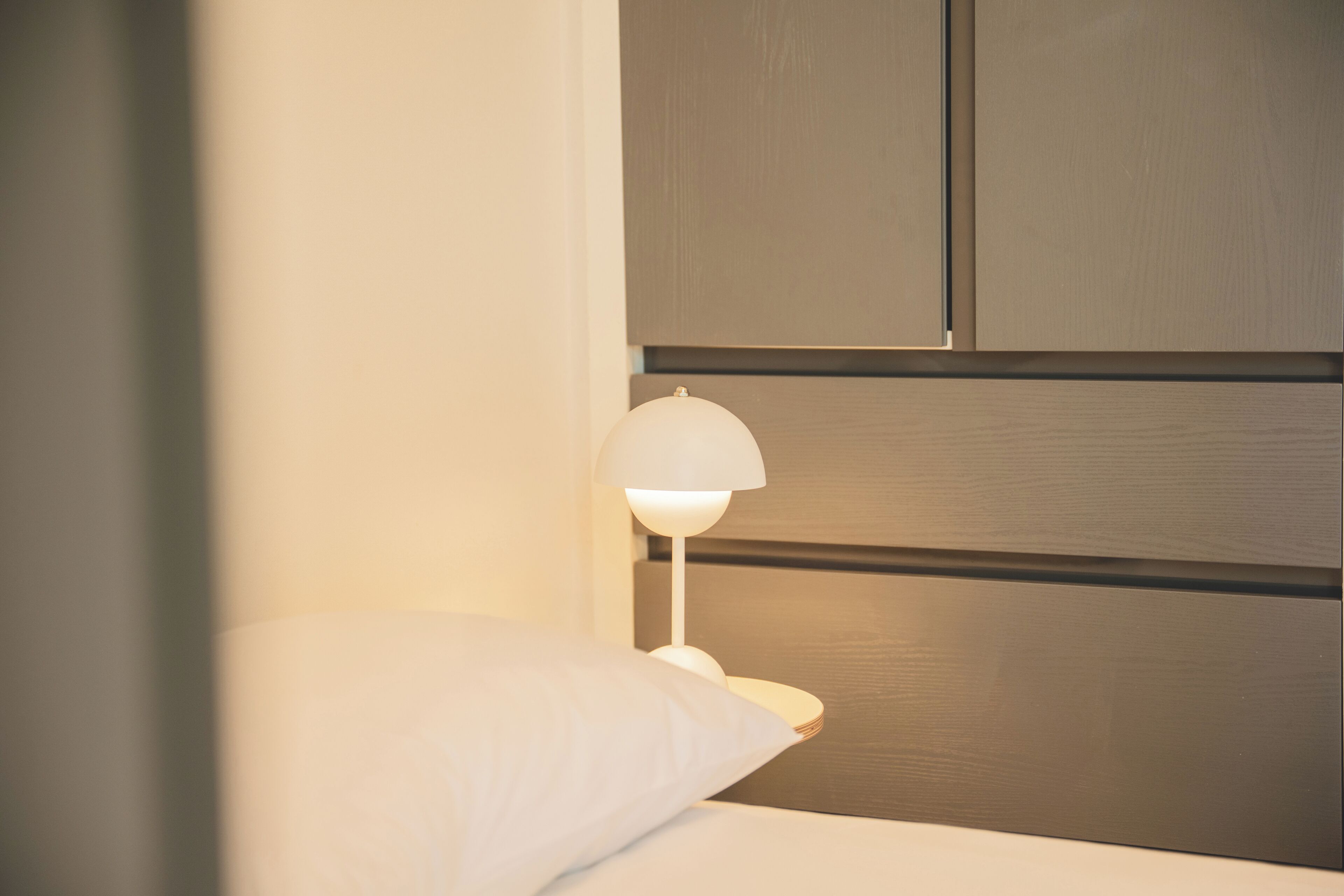 A neatly made bed with a white pillow and a white bedside lamp.