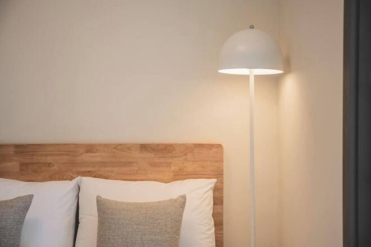 Un lit avec une tête de lit en bois, des oreillers blancs et gris, et une lampe de sol blanche.