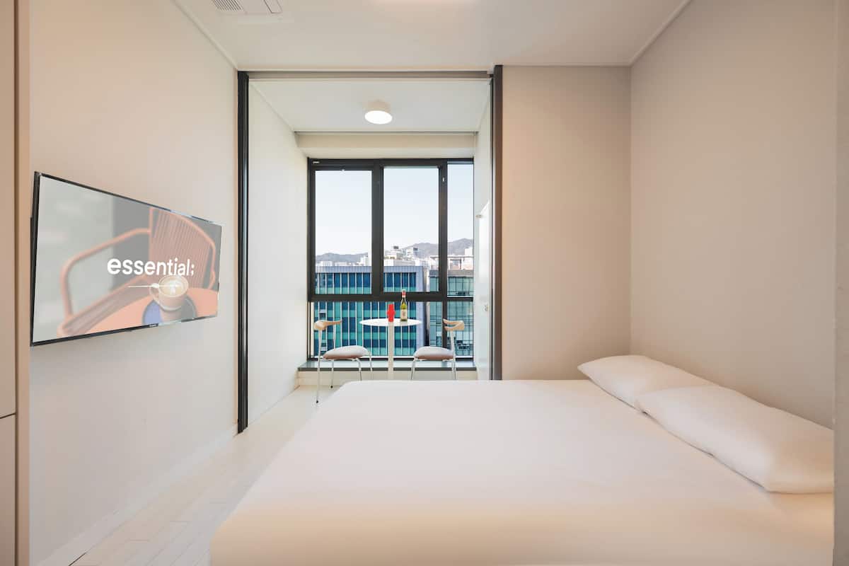 Une chambre d’hôtel moderne avec un grand lit, un téléviseur fixé au mur et un balcon équipé d’une table et de chaises.