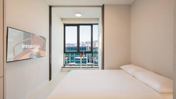 A modern hotel room with a large bed, a TV on the wall, and a balcony with a table and chairs.