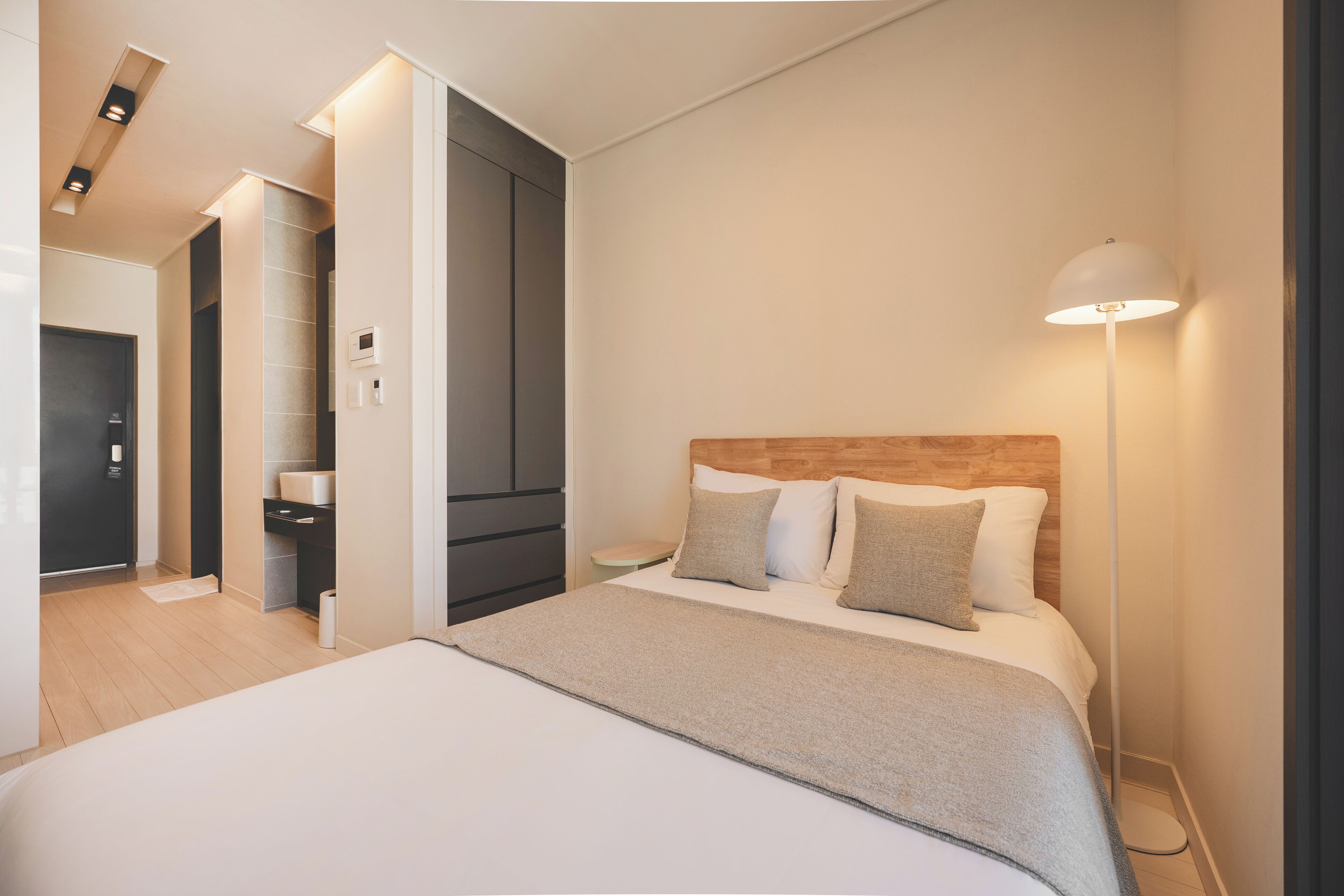 A modern hotel room with a large bed, a wooden headboard, a bedside lamp, and a walk-in closet.