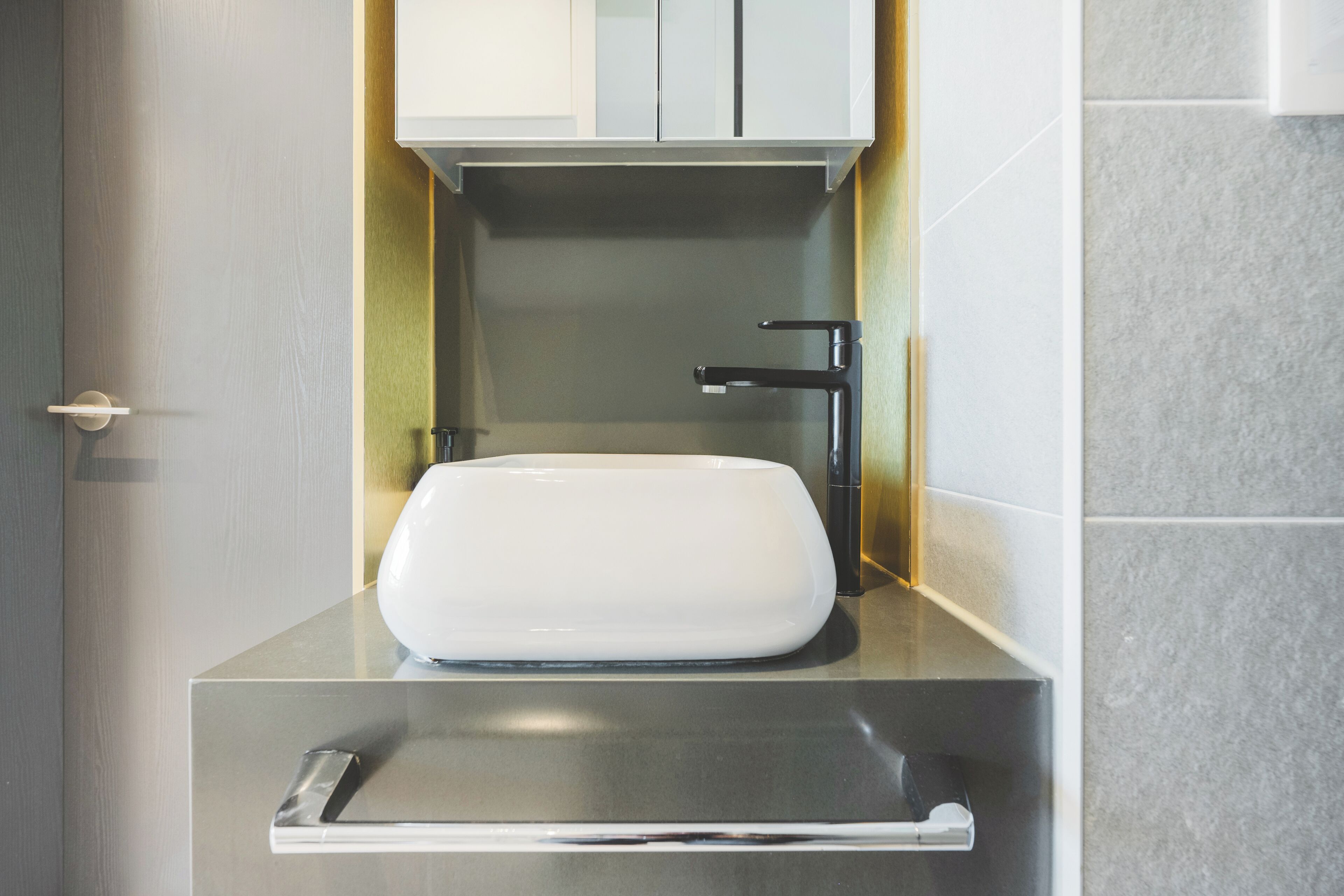 A modern bathroom with a white sink, a black faucet, and a stainless steel countertop.