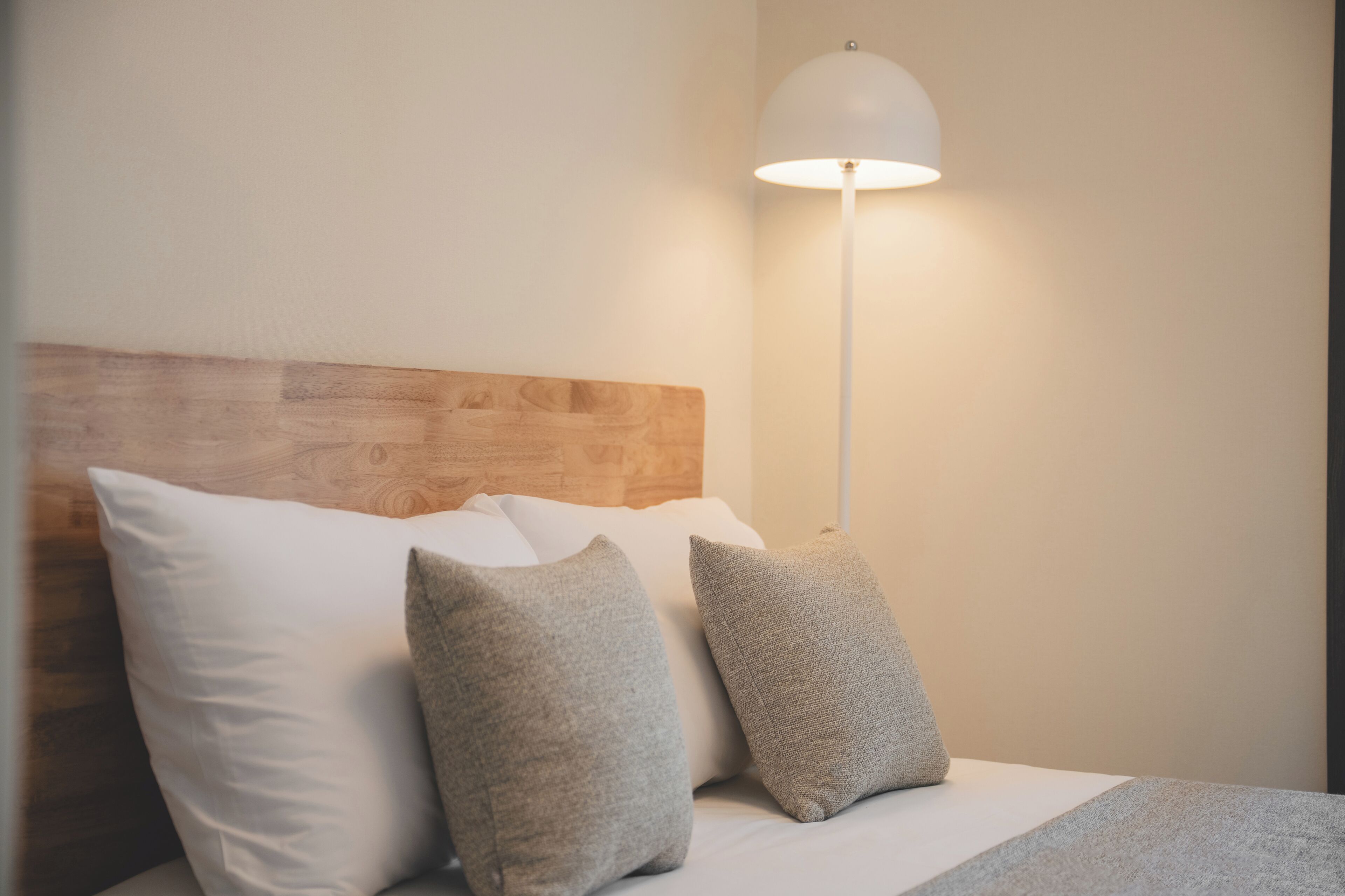 A bed with a wooden headboard, white and grey pillows, and a white floor lamp.