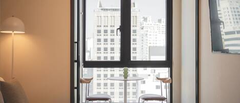A hotel room with a large window, a bed, two chairs, a small table, and a lamp.