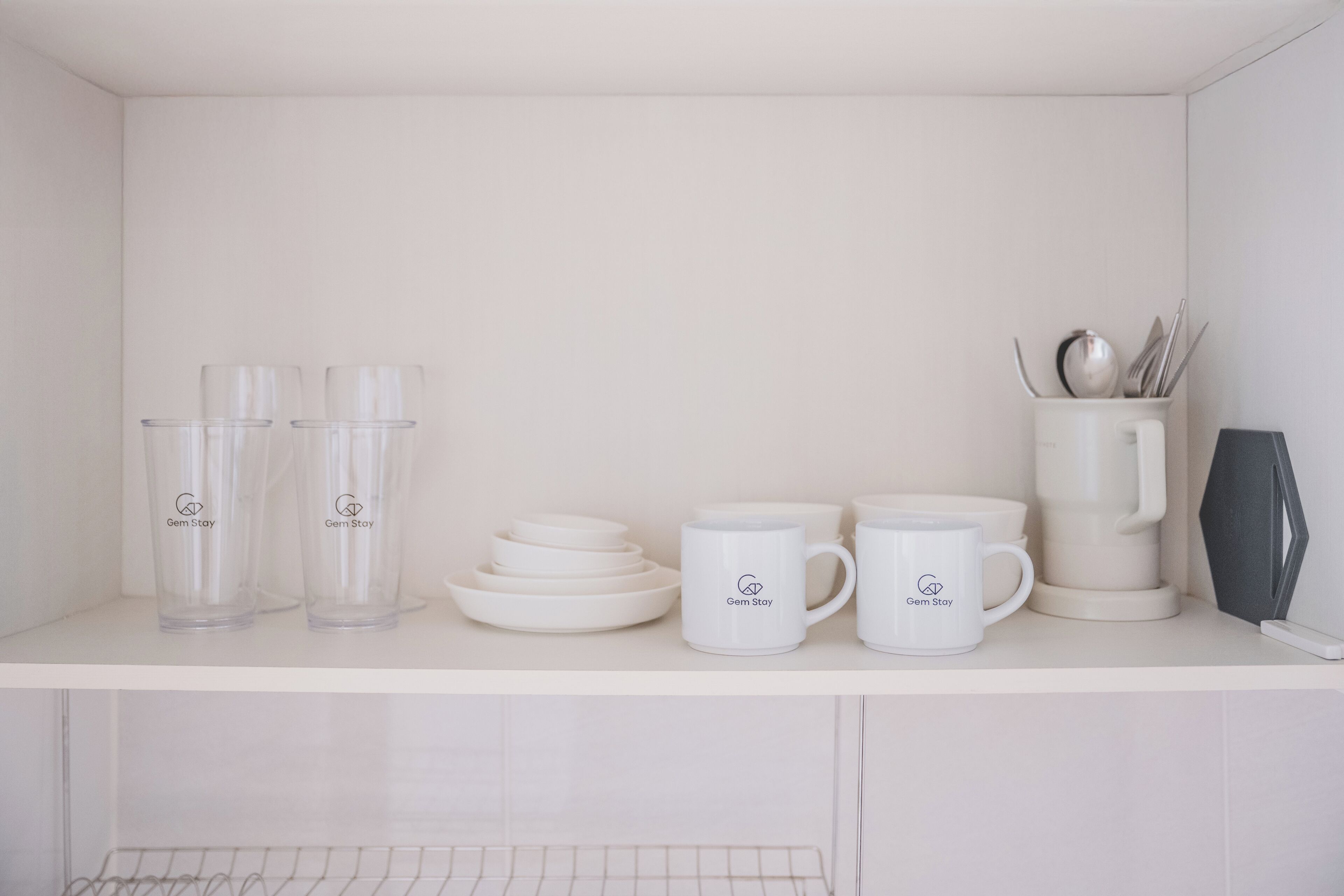 A white kitchen counter with clear glass tumblers, white plates, a white mug, and a white coffee maker.