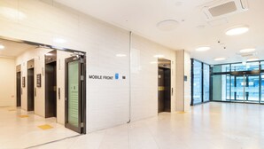 A modern lobby with a mobile front elevator, glass doors, and a tiled floor. - Gemstay Seomyeon (Busan)
