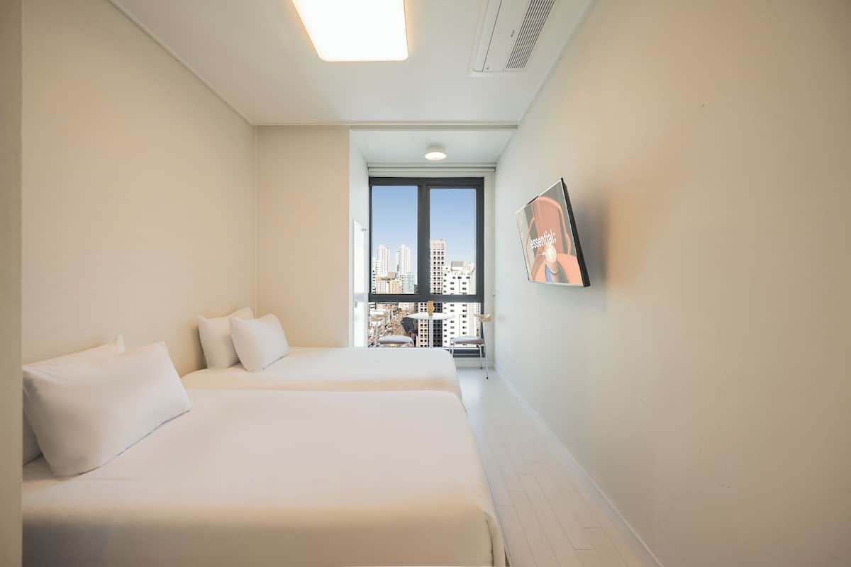 Une chambre d’hôtel avec deux lits, une grande fenêtre donnant sur la ville et un téléviseur fixé au mur.