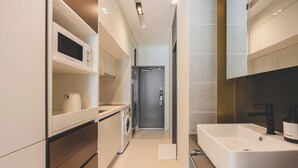 A modern kitchen with a built-in microwave, a washing machine, and a large white sink. - Gemstay Seomyeon (Busan)