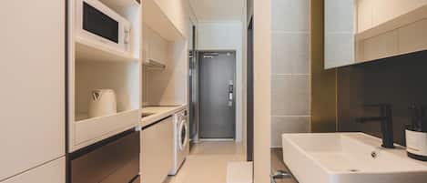 A modern kitchen with a built-in microwave, a washing machine, and a large white sink.