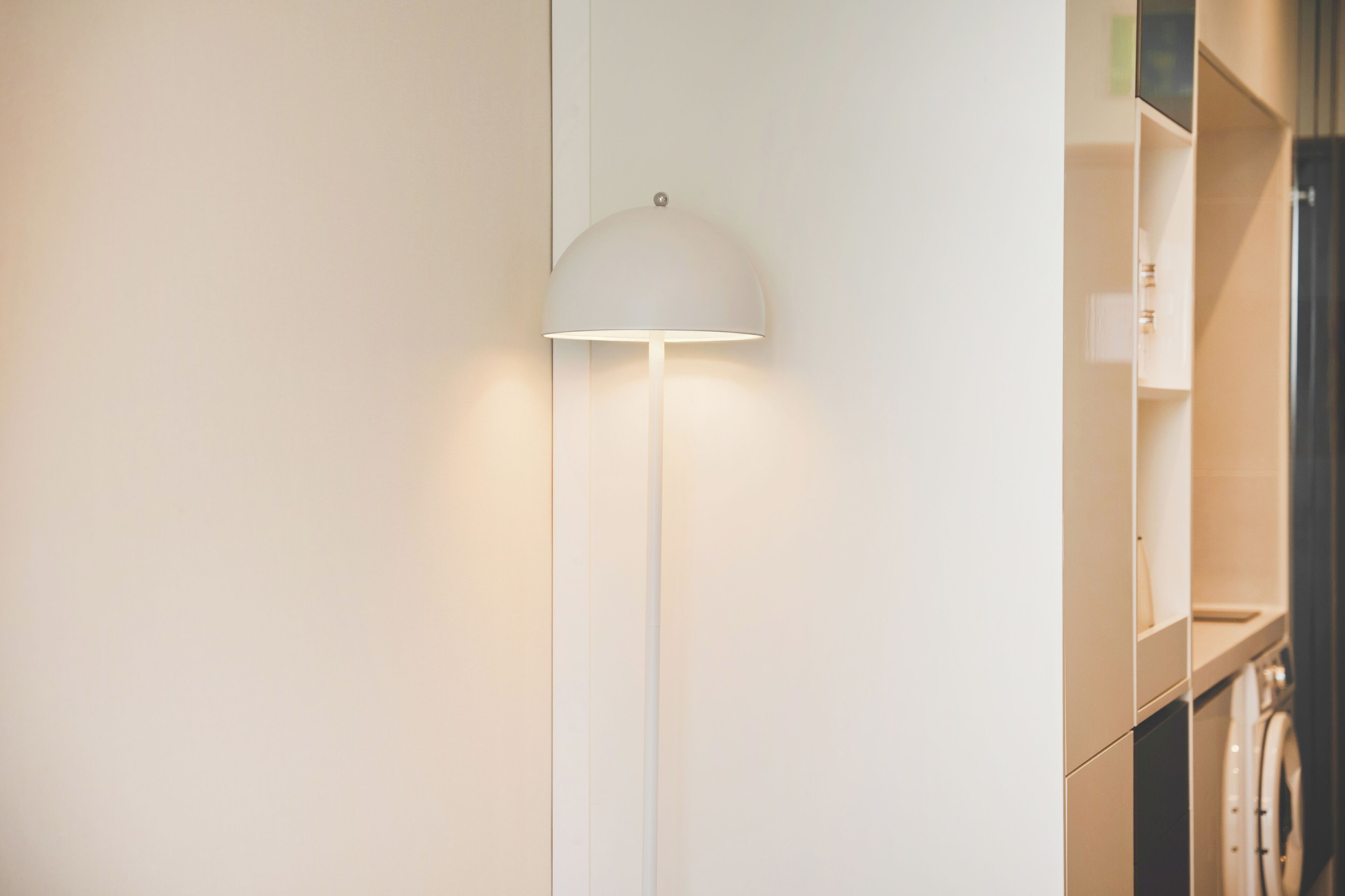 A modern, minimalist room with a white floor lamp and a built-in washing machine.
