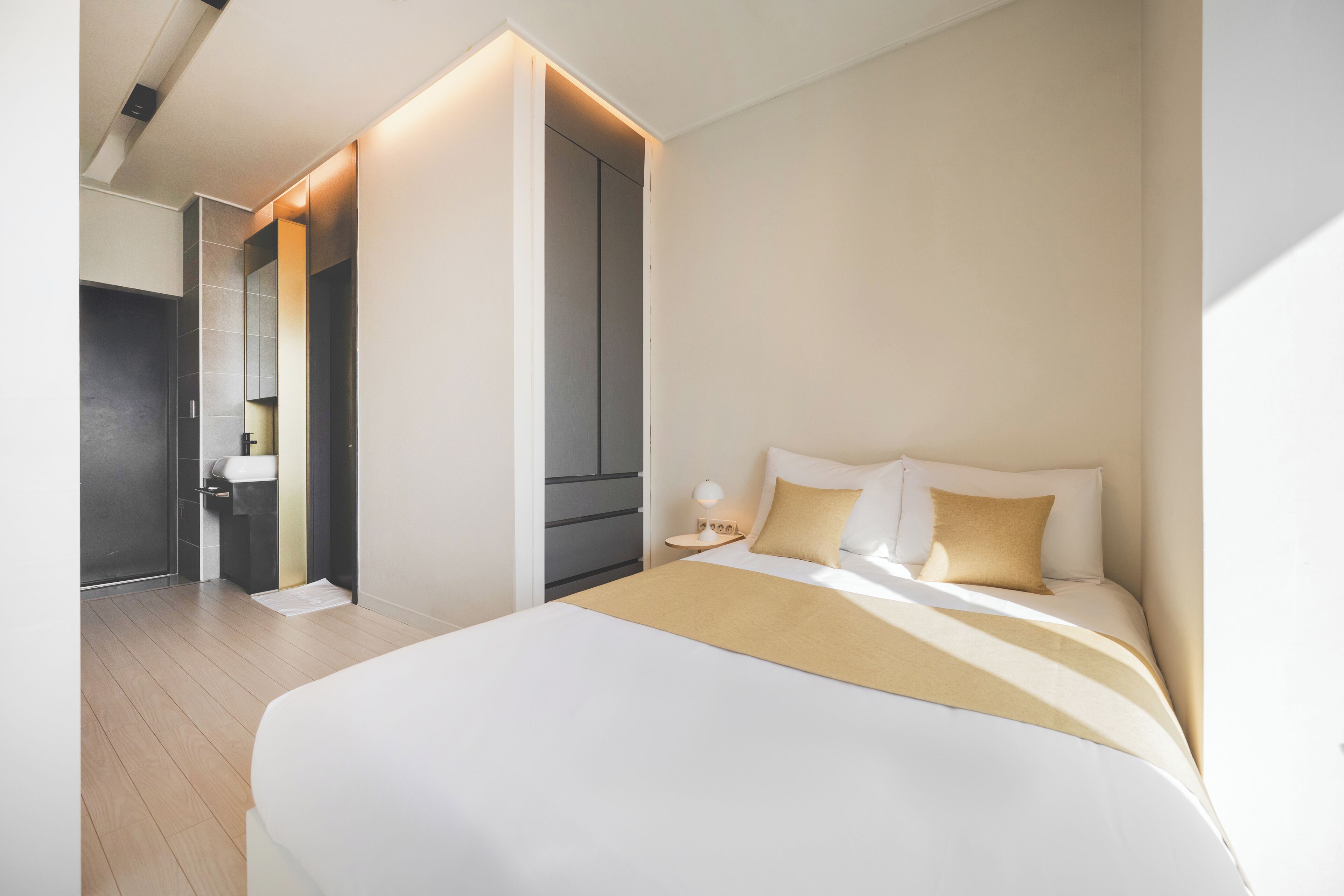 Quarto de hotel moderno com uma cama grande, mesa de cabeceira com abajur e closet espaçoso.