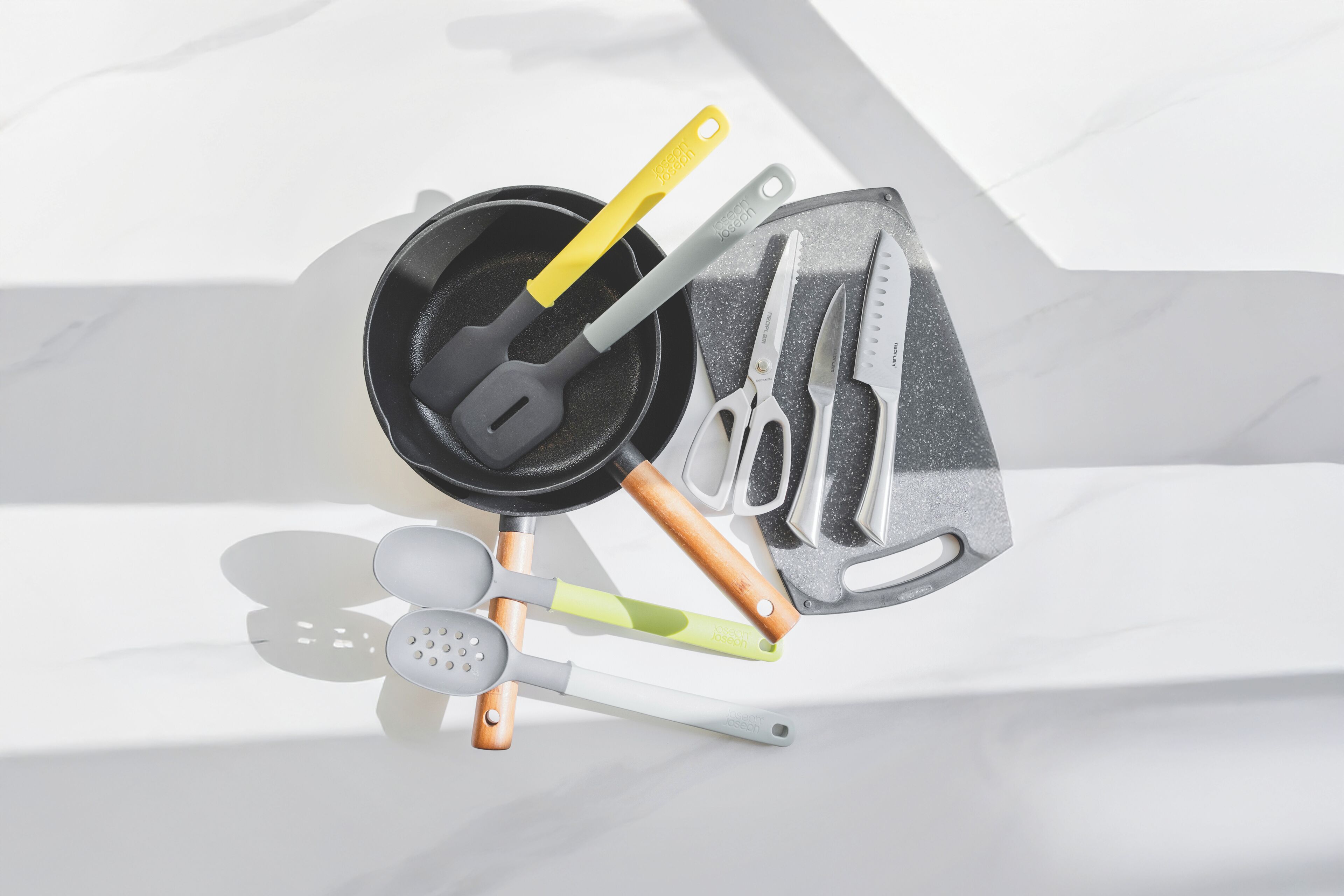 A kitchen with a black frying pan, a yellow spatula, a green spatula, a pair of scissors, and a knife set.