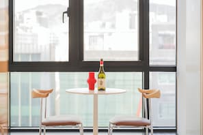 A room with a round table, two chairs, a bottle of wine, and a red vase.