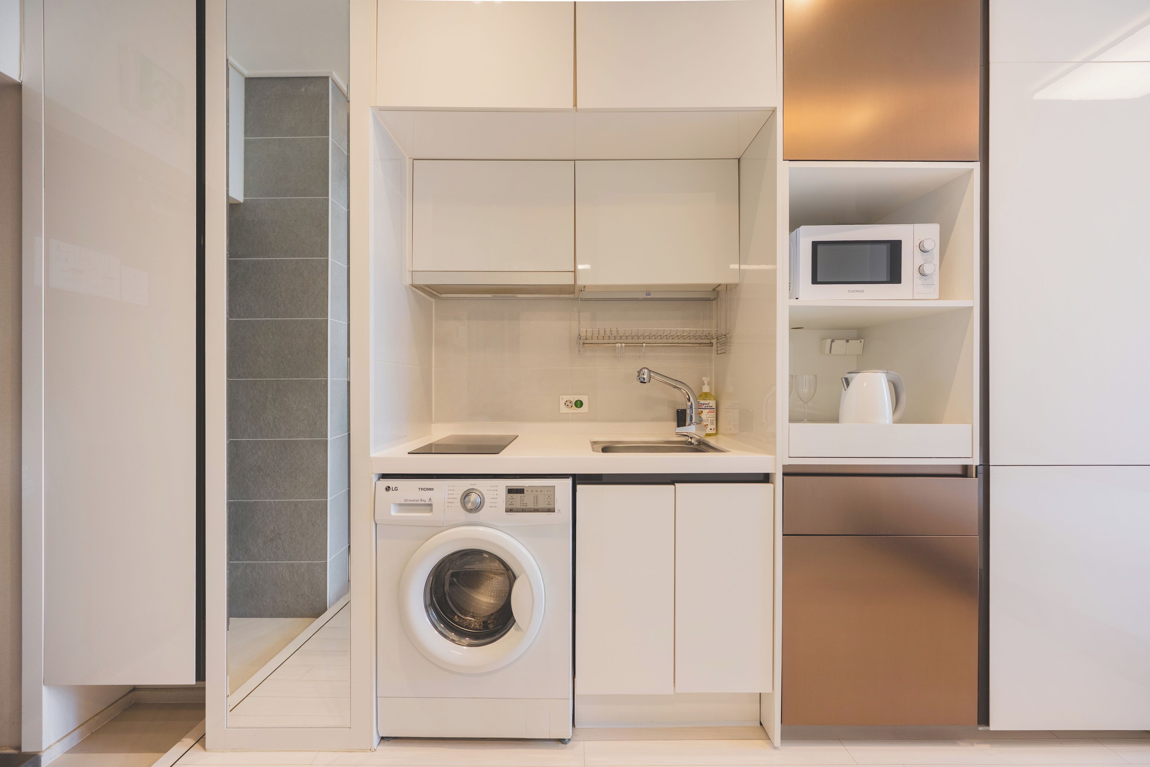 A compact kitchen with a washing machine, microwave, and built-in oven.