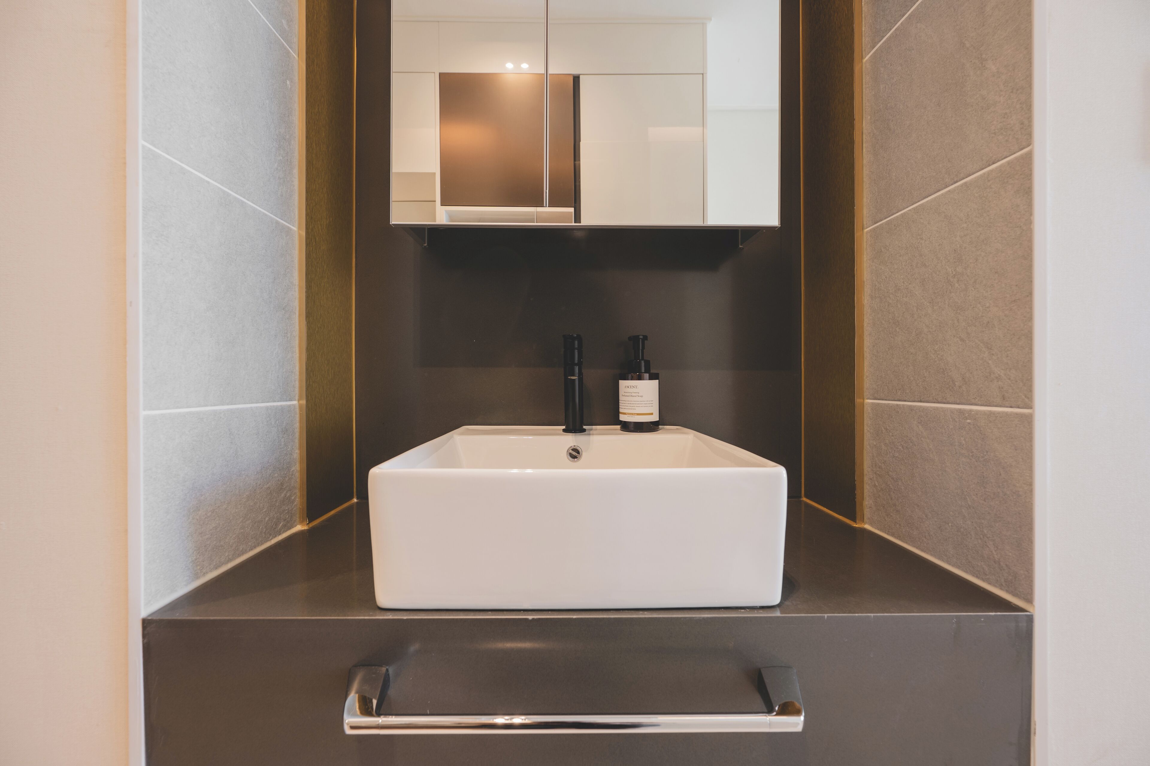 A modern bathroom with a rectangular sink, a mirror above it, and a towel rack below.