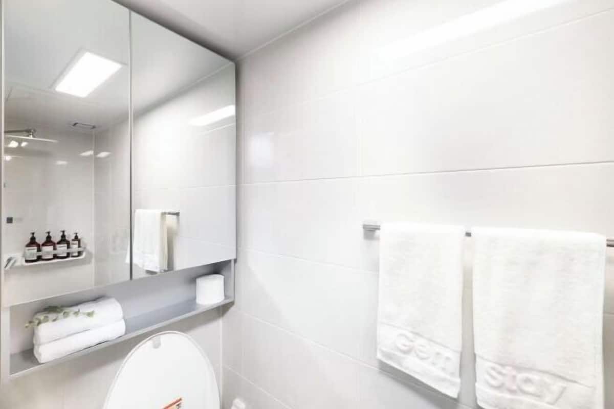 Une salle de bain moderne équipée de toilettes, d’un miroir et d’une étagère où sont rangés les articles de toilette.