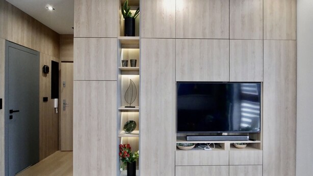 A modern living room with a built-in TV, wooden paneling, and shelves with decorative items.