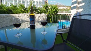 Une table en verre avec deux verres à vin et une bouteille de vin, une chaise, et une piscine en arrière-plan.
