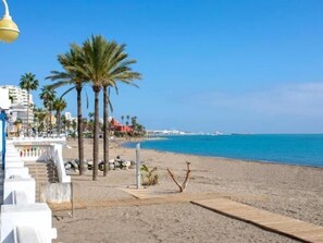A beach with palm trees, a clear blue sky, and a building with a red roof in the background. - Sunstay Relax 54 Rio Marina Nerja (Nerja)