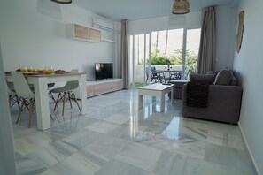 A modern living room with a dining area, a flat-screen TV, and a balcony with a view. - Sunstay Relax 54 Rio Marina Nerja (Nerja)