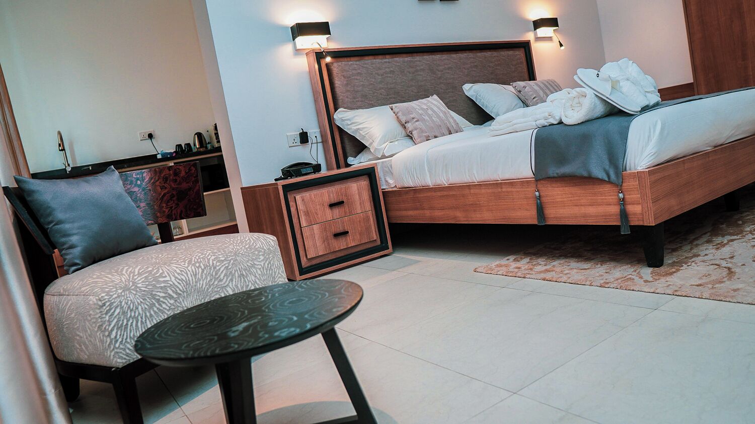 A modern bedroom with a wooden bed, bedside tables, a chair, and a small round table.