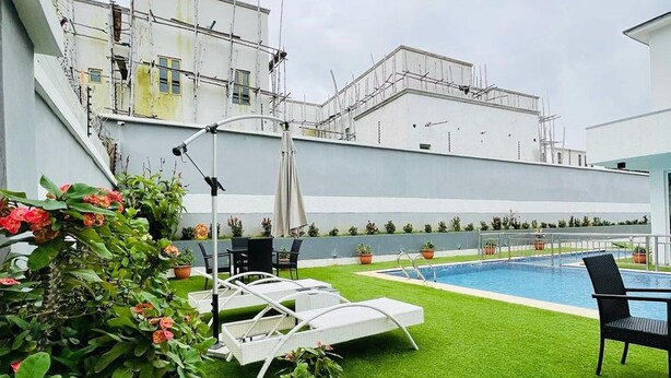 Un espace piscine aménagé sur le toit, avec du gazon synthétique, des chaises longues et des plantes en pot.