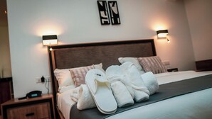 Un lit bien fait, avec des serviettes et des chaussons blancs, une table de chevet en bois avec un téléphone et des lampes fixées au mur.