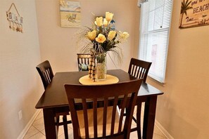 A dining table with chairs, a vase with flowers, and a beach-themed wall decoration.