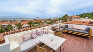 A rooftop terrace with a seating area, a table, and a view of the sea and cityscape. - Ajlan Beach (Ayvalik)