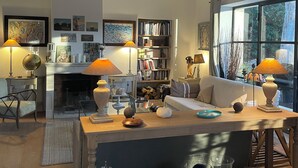 A cozy living room with a fireplace, bookshelves, and a large window. - Saint Rémy de Provence -mas de Charme à 3 Km du Centre (Saint-Rémy-de-Provence)
