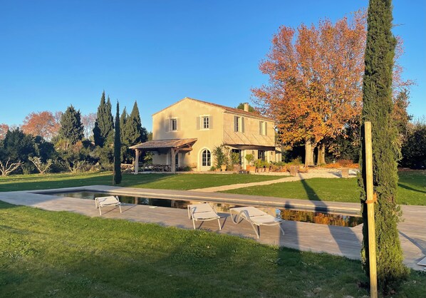 Una casa grande con piscina, mobiliario de exterior y un jardín bien cuidado.