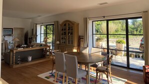 A spacious living area with a dining table, chairs, a cabinet, and large windows offering a view of the outdoors. - Saint Rémy de Provence -mas de Charme à 3 Km du Centre (Saint-Rémy-de-Provence)